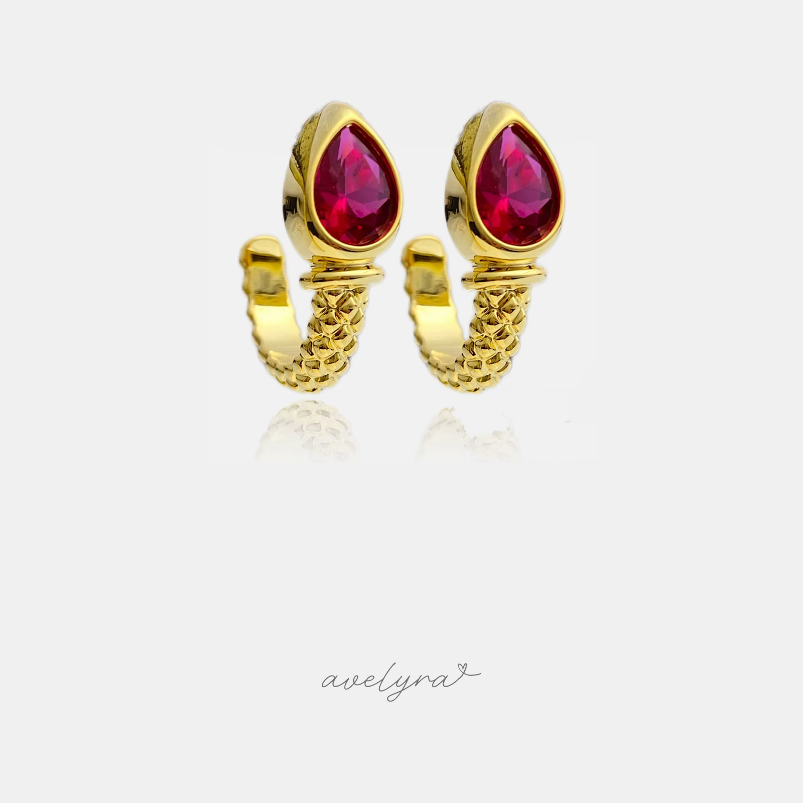 Gold-tone huggie earrings with faceted crimson-pink pear-shaped stone and rope-textured band.
