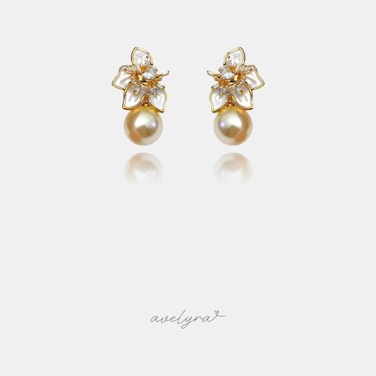 Gold-tone earrings with a white pearlescent petal flower and crystal centre above a golden round pearl.