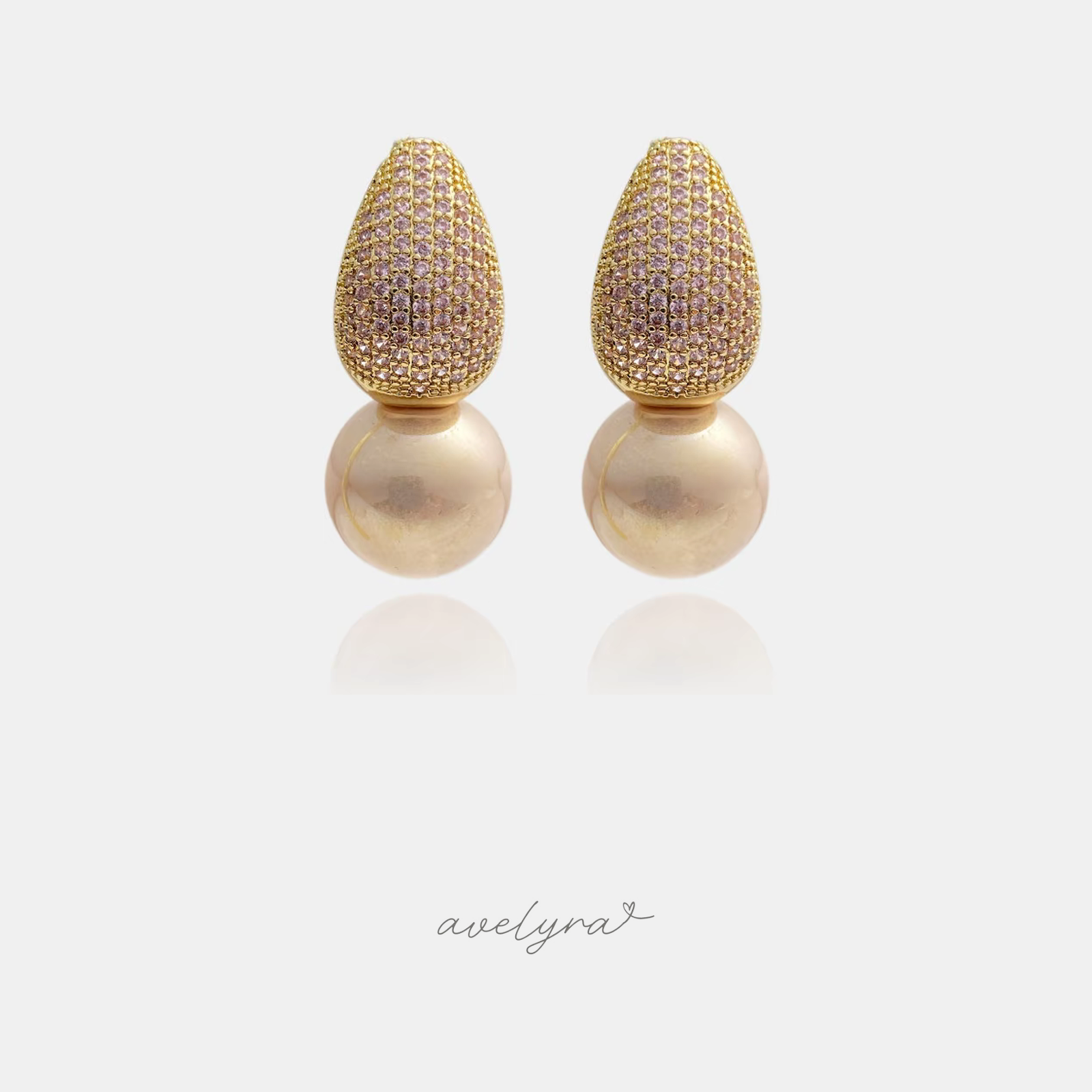 Gold pavé teardrop earrings with blush stones above a large rounded pearl.