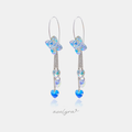 Pair of silver-tone hook earrings with an iridescent butterfly and chains holding heart-shaped crystals ending in a blue heart stone.