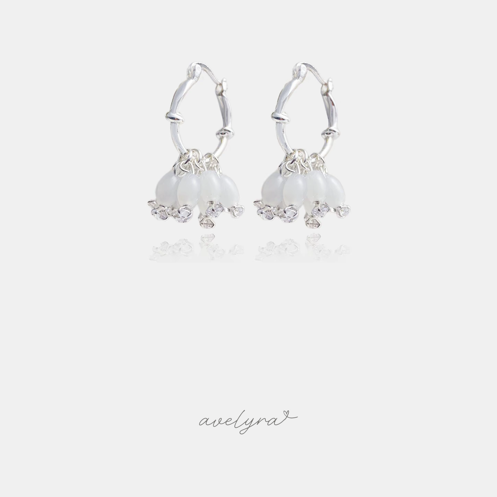 Pair of silver-tone hoop earrings with a cluster of milky white bell-shaped beads and small clear accent stones.