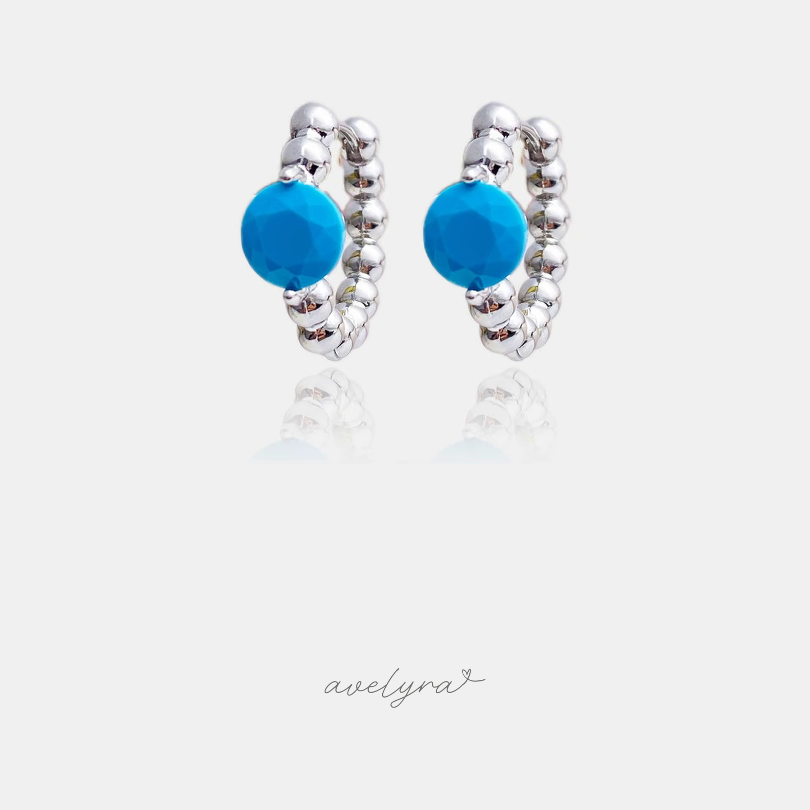 Silver-tone beaded huggie earrings each set with a faceted turquoise-blue round stone.