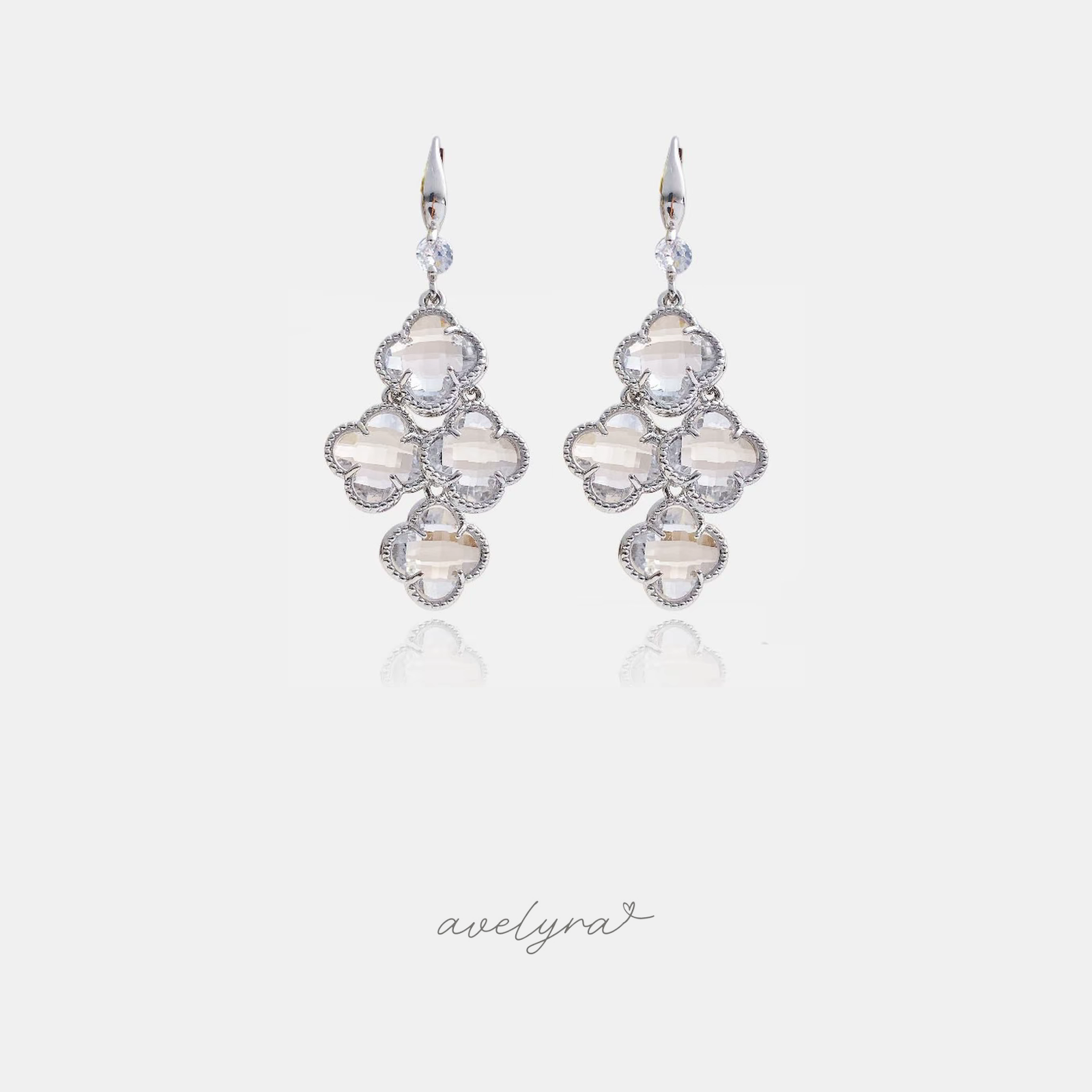 Silver-tone drop earrings with clusters of clear faceted quatrefoil clover-shaped stones on a hook fitting.