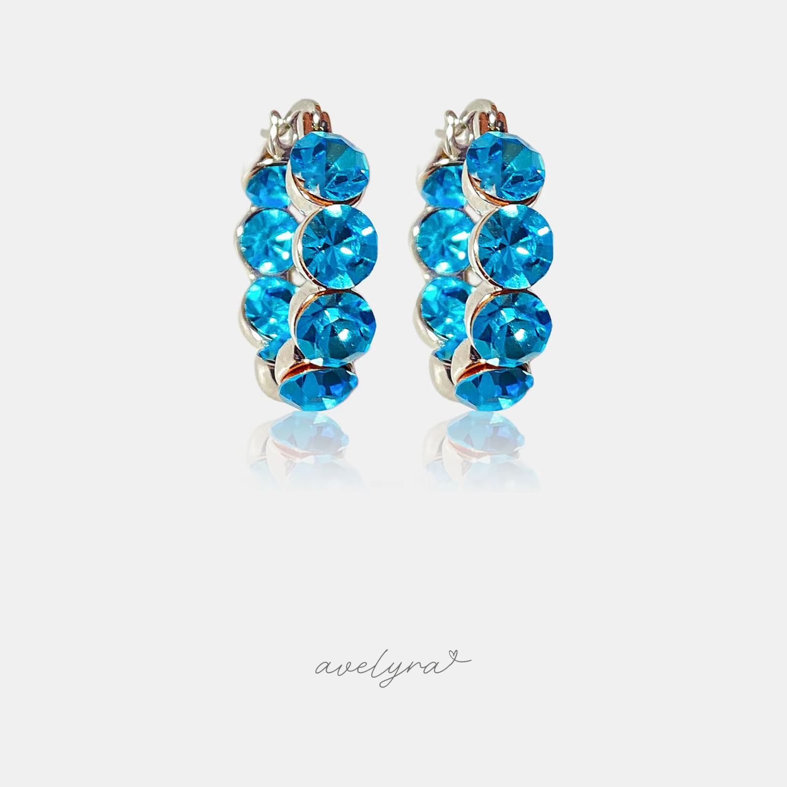Pair of small silver huggie hoop earrings set with a row of round aqua-blue crystals.
