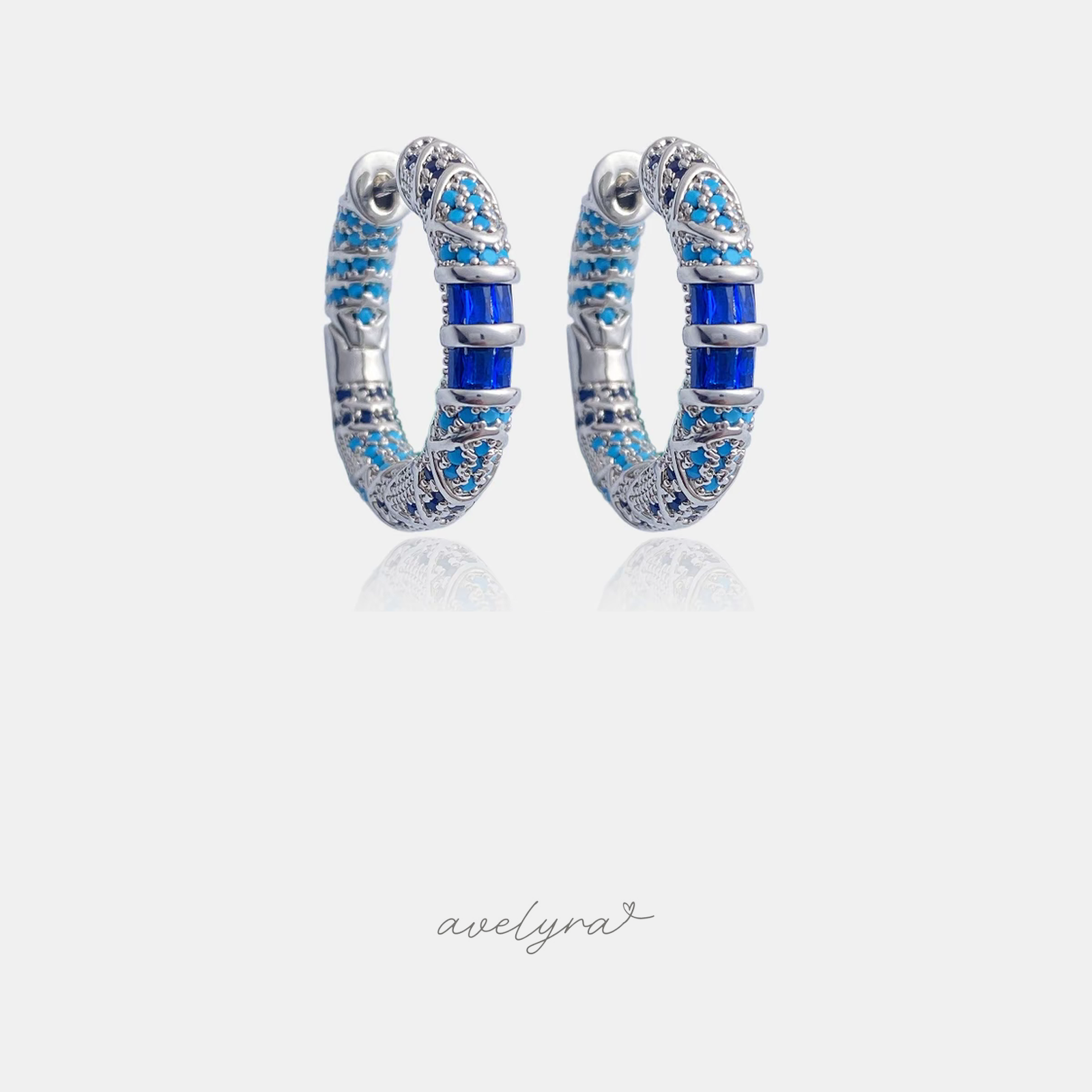 Silver-tone hoop earrings paved in turquoise and dark blue stones with a central cobalt baguette crystal.