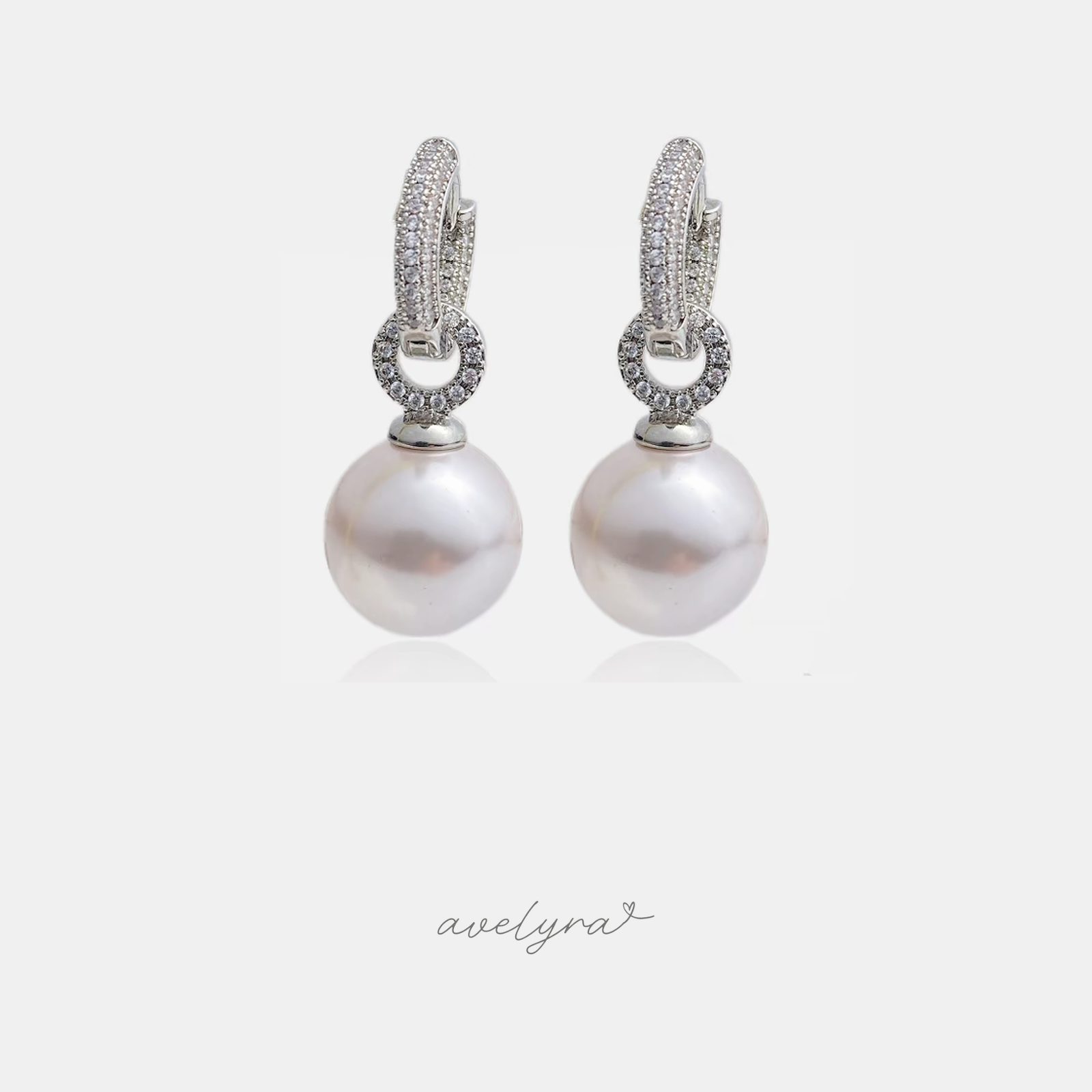 Drop earrings with a large white pearl suspended below a pave crystal ring and huggie hoop top.