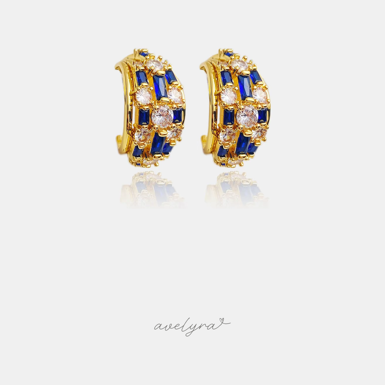 Gold-tone curved huggie hoop earrings set with deep blue baguette and clear round crystals.