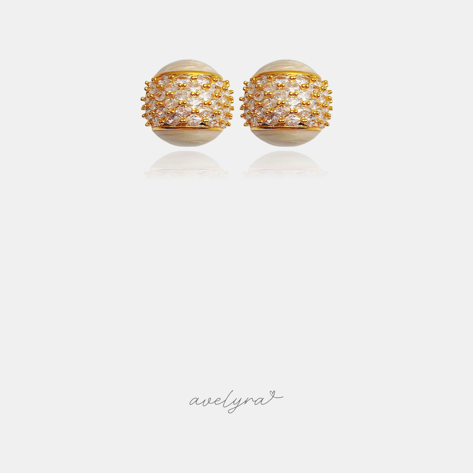 Domed stud earrings with cream pearl-sheen surface and a central band of clear stones in gold prongs.