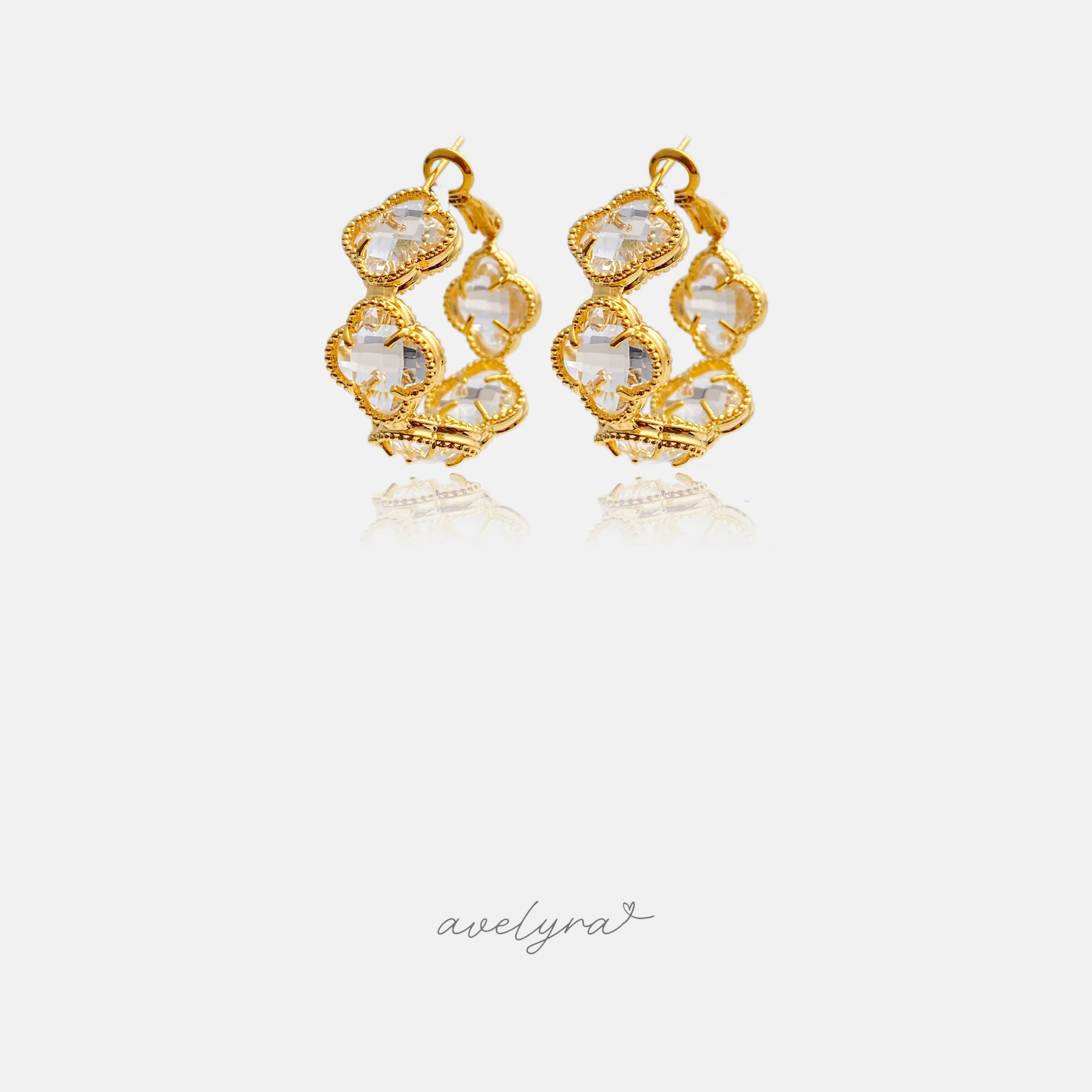 Gold clover-motif hoop earrings set with clear faceted stones.