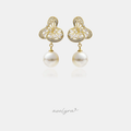 Gold filigree drop earrings set with clear stones above a large hanging white pearl.