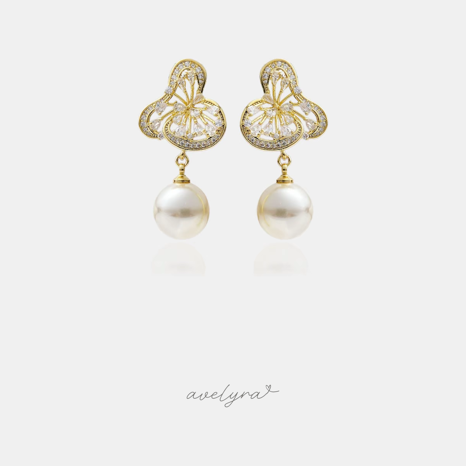 Gold filigree drop earrings set with clear stones above a large hanging white pearl.