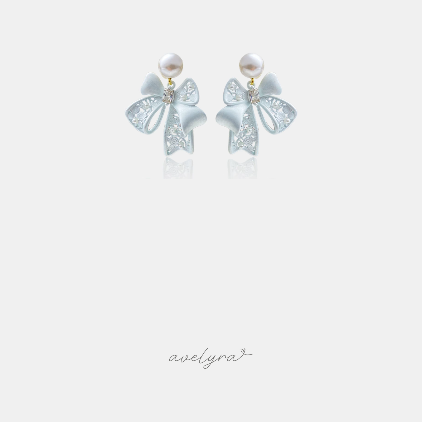 Powder-blue openwork bow earrings with a clear centre stone hanging beneath a white pearl.