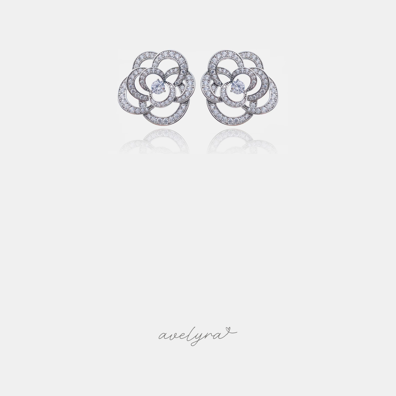 Pair of silver-tone camellia flower stud earrings with swirling pave clear stones around a central round stone.