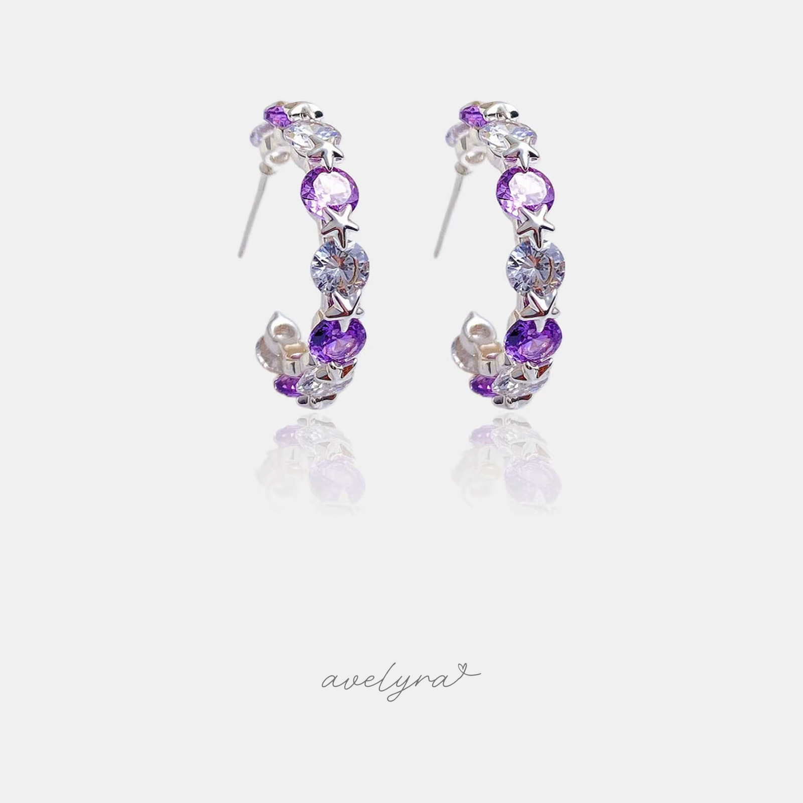 Pair of silver-tone hoop earrings set with alternating violet and clear round crystals and small star shapes.