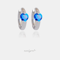 Pair of silver-tone huggie hoop earrings each set with a single blue heart-shaped crystal.