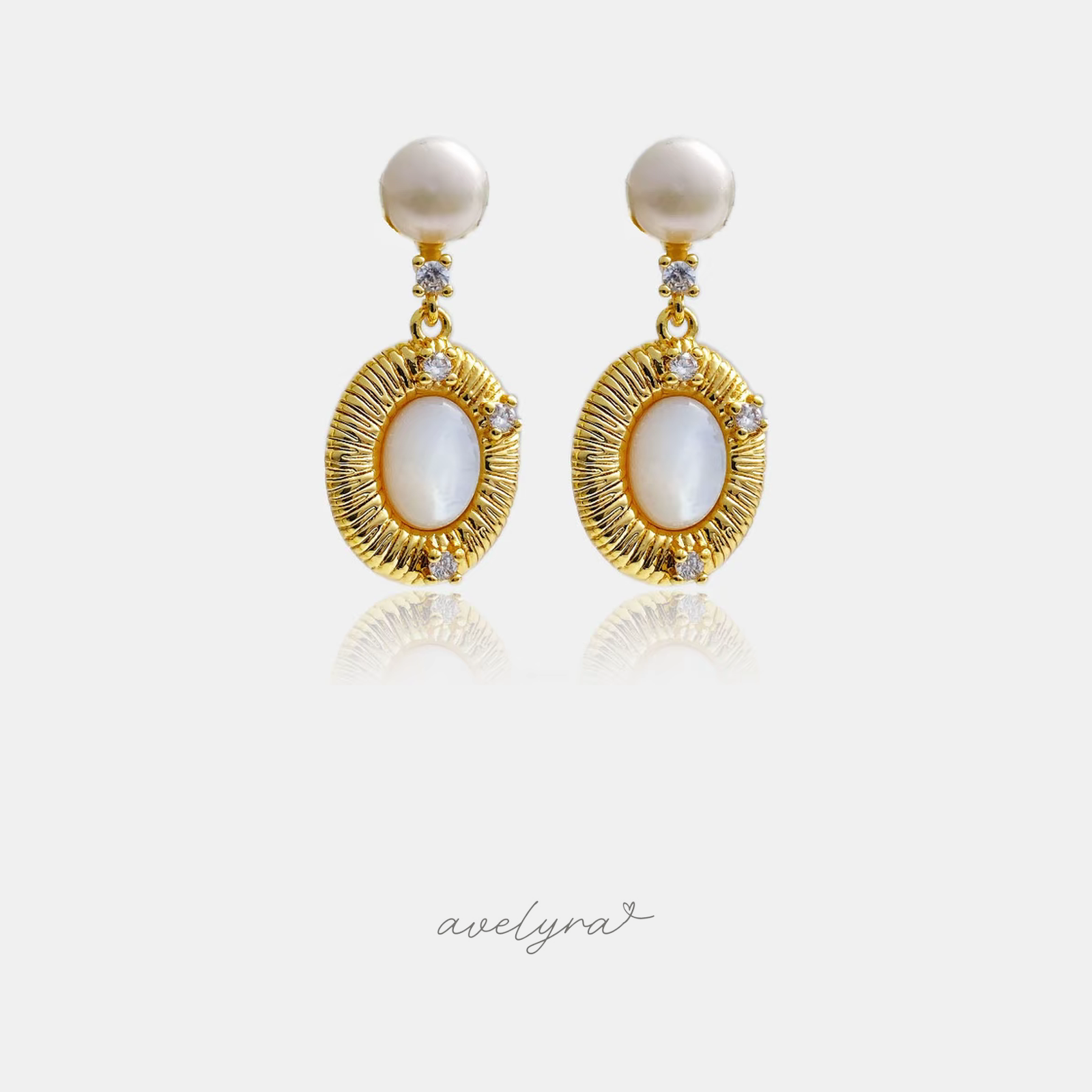 Pair of gold-tone drop earrings with a round pearl top and a ridged sunburst frame around an oval pearly cabochon.