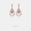 Pair of gold-tone drop earrings with a violet teardrop crystal above a crescent of milky white stones and clear crystals.