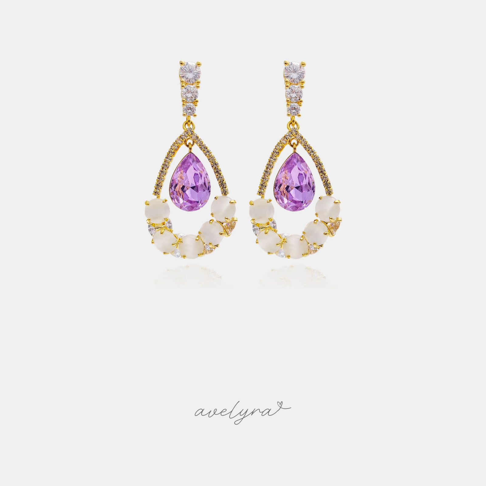 Pair of gold-tone drop earrings with a violet teardrop crystal above a crescent of milky white stones and clear crystals.
