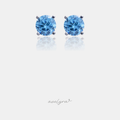 Pair of silver-tone stud earrings each set with a round faceted sky-blue stone in a four-prong setting.