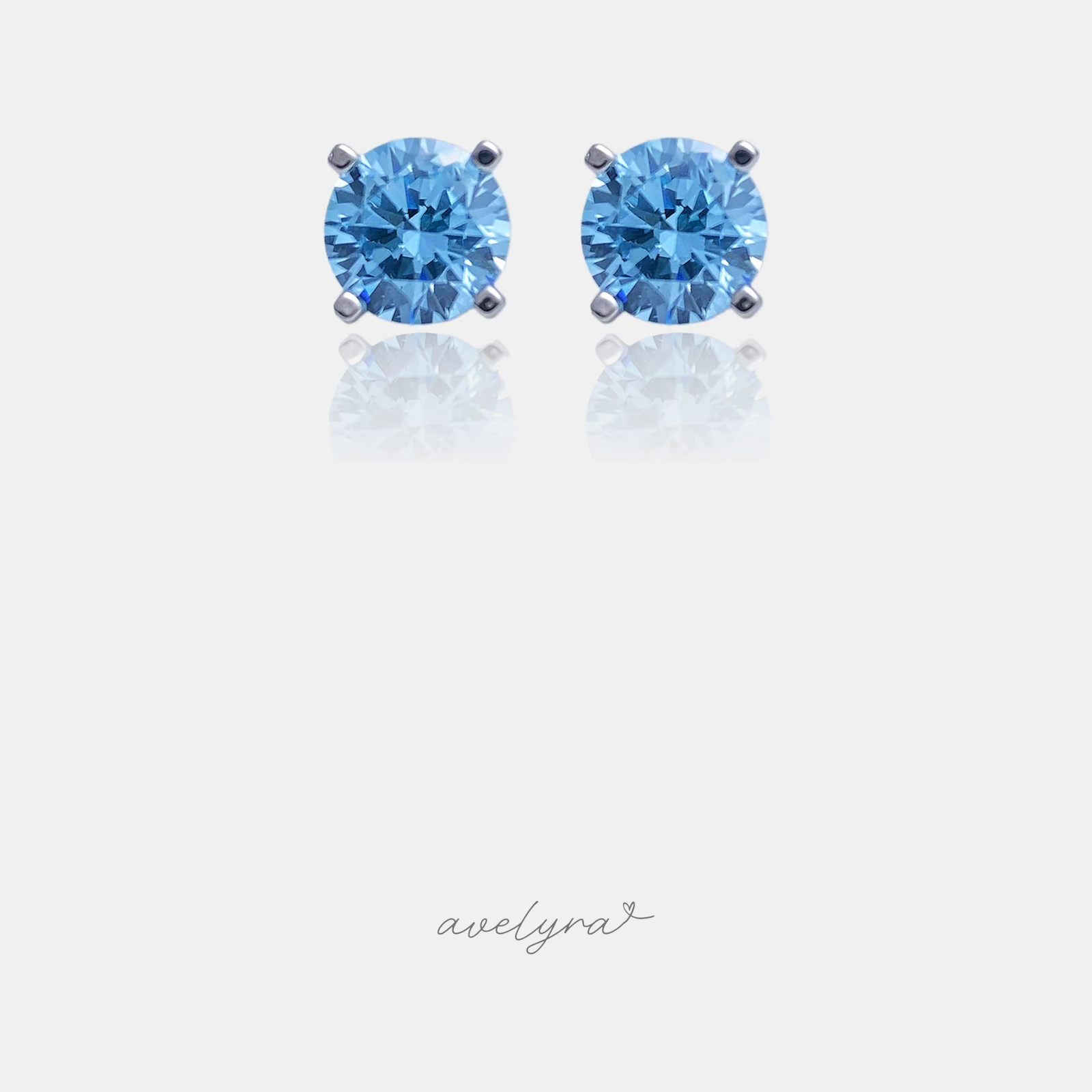 Pair of silver-tone stud earrings each set with a round faceted sky-blue stone in a four-prong setting.