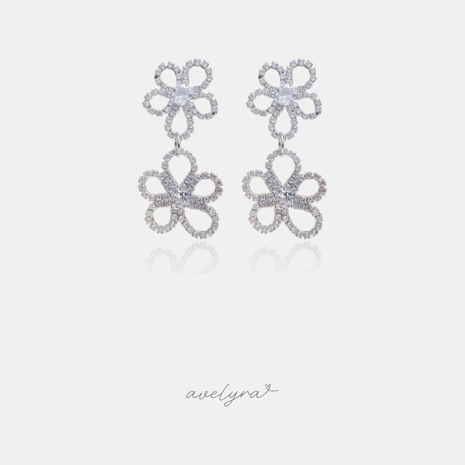 Silver-tone earrings with two openwork pave flowers, each with a clear round stone at the centre, hanging one below the other.