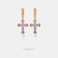 Gold-tone huggie hoop earrings each with a hanging cross set with clear round stones.
