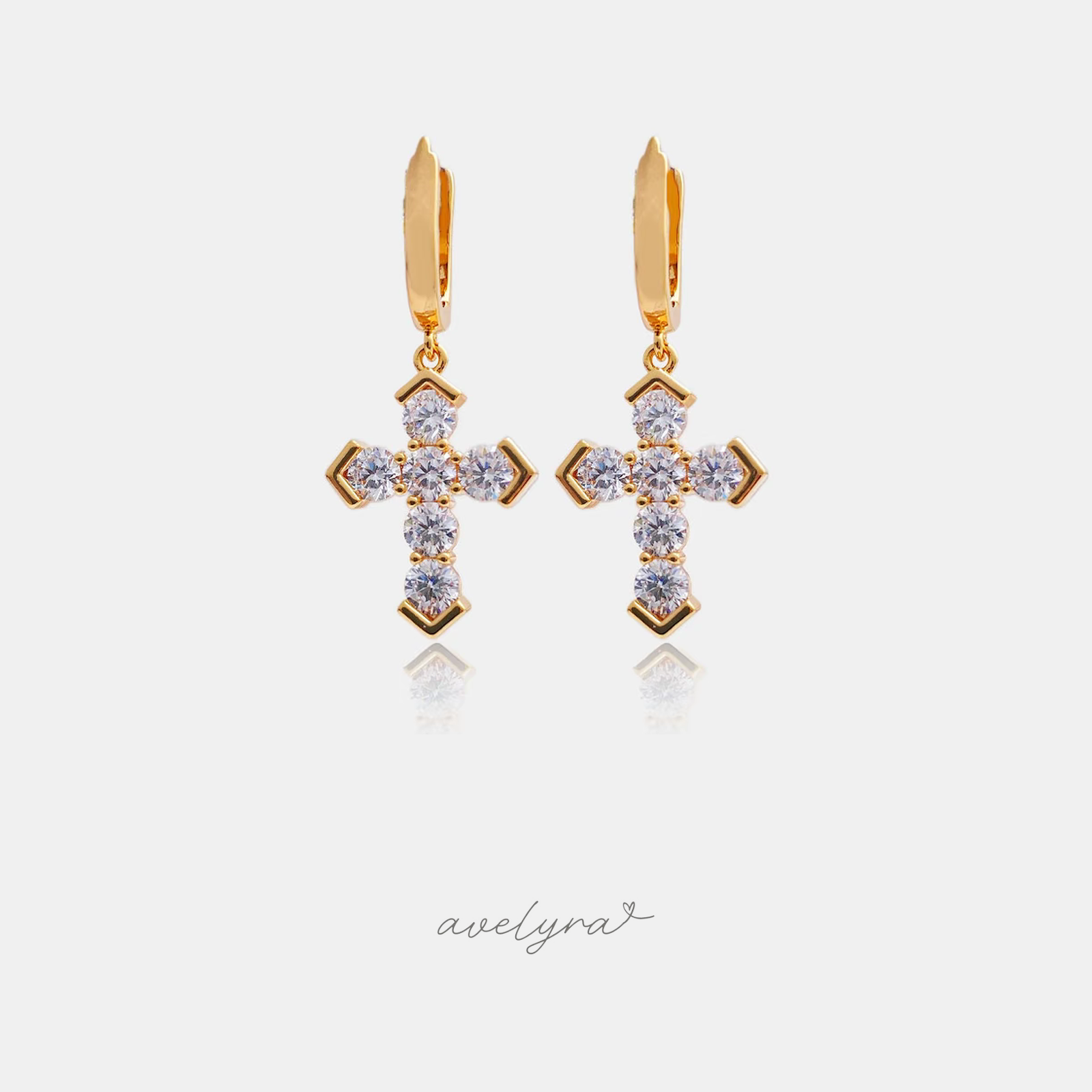 Gold-tone huggie hoop earrings each with a hanging cross set with clear round stones.