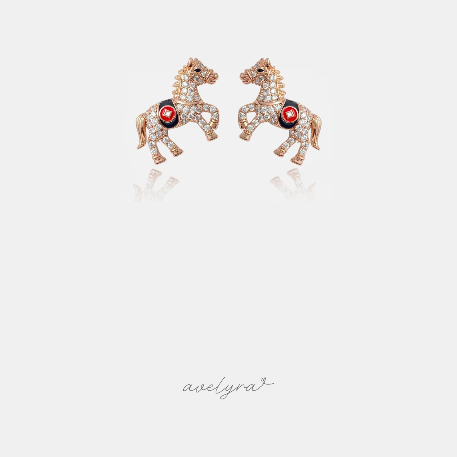 Rose gold-tone horse stud earrings paved with clear stones and red and black accents.