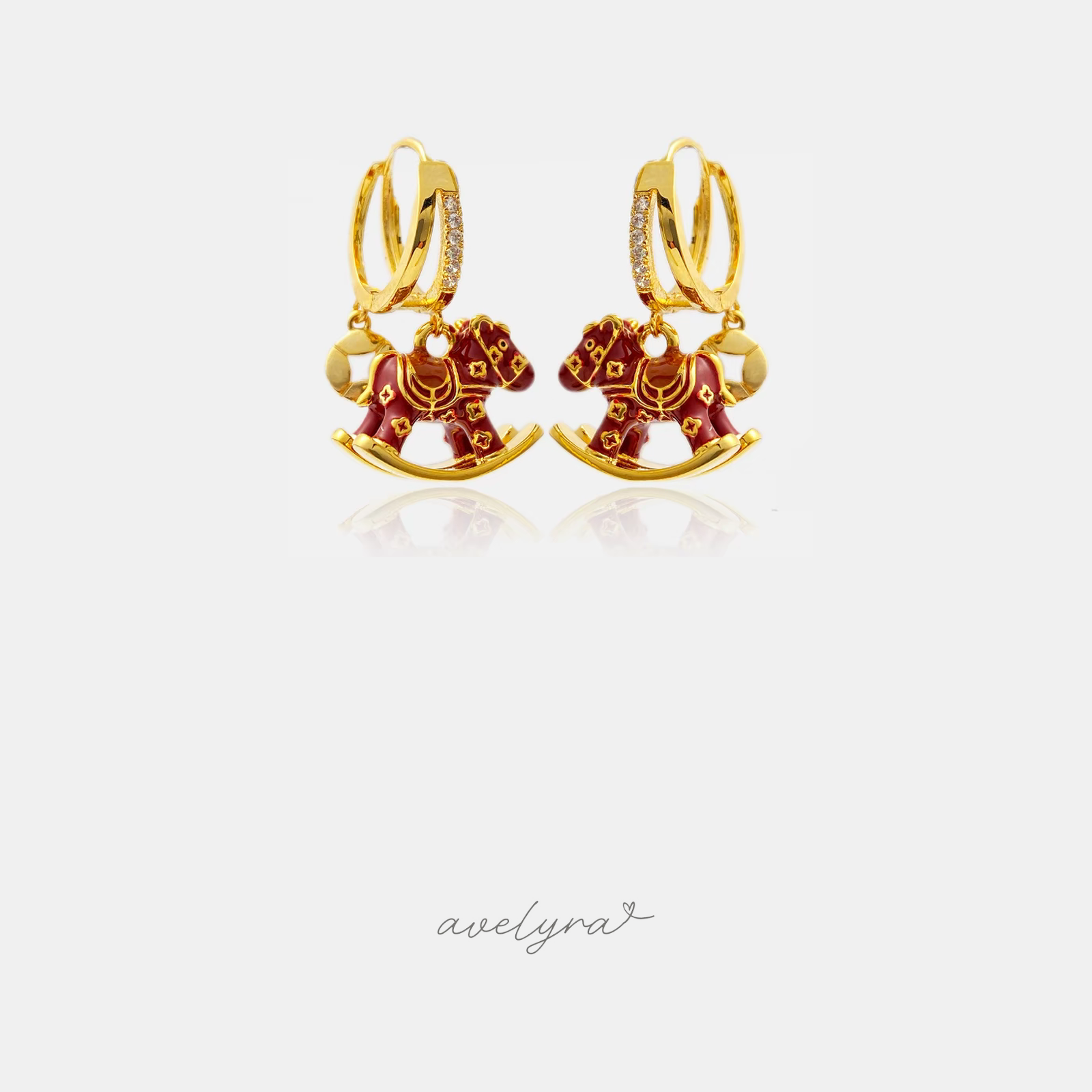 Gold-tone huggie earrings with a red enamel rocking-horse charm.