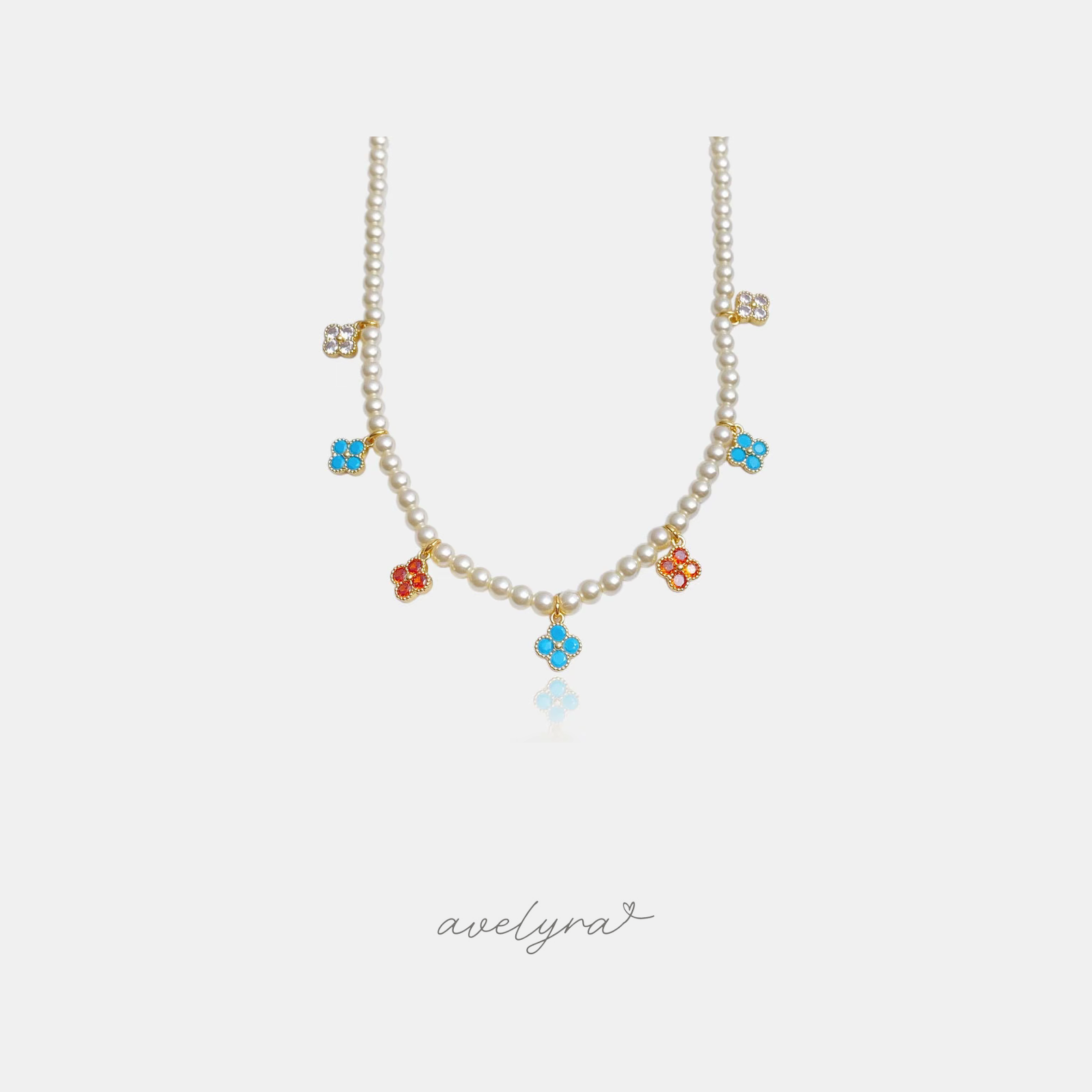 Pearl necklace with dangling four-petal clover charms in turquoise, red and clear crystal set in gold.