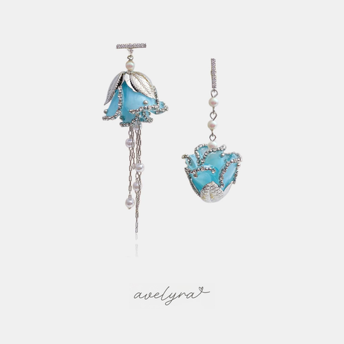 Mismatched silver-tone drop earrings with pale blue flower blooms outlined in clear crystals, small white pearls and a fine chain tassel on one side.