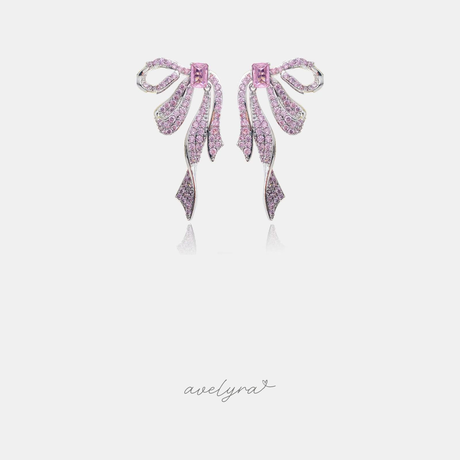 Silver-tone bow earrings covered in pink crystals with a central pink stone and long ribbon-like dangles.