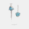 Asymmetric blue flower earrings, one with pearl-dotted chain tassels and one cupped in silver leaves.