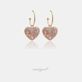 Gold-tone twisted hoop earrings each holding a puffed heart charm paved with pink crystals.