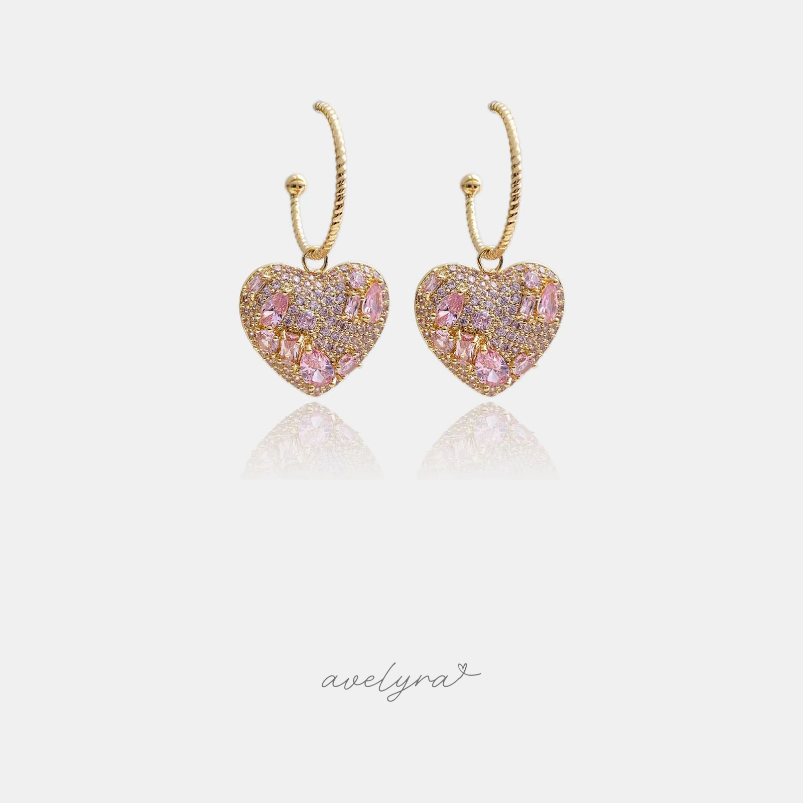 Gold-tone twisted hoop earrings each holding a puffed heart charm paved with pink crystals.