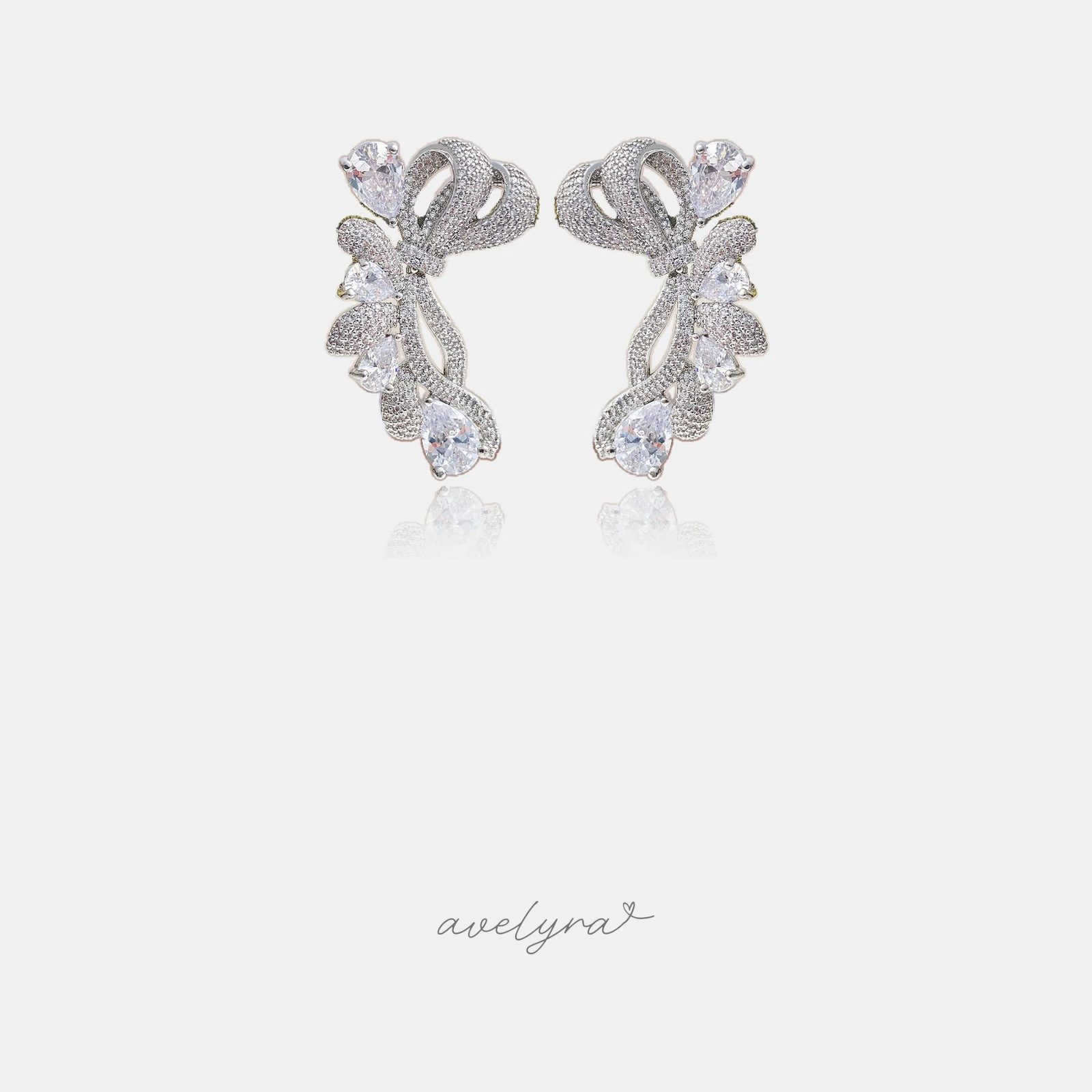 Silver-tone bow-shaped earrings covered in small clear stones with larger clear pear-cut stones along the sides.