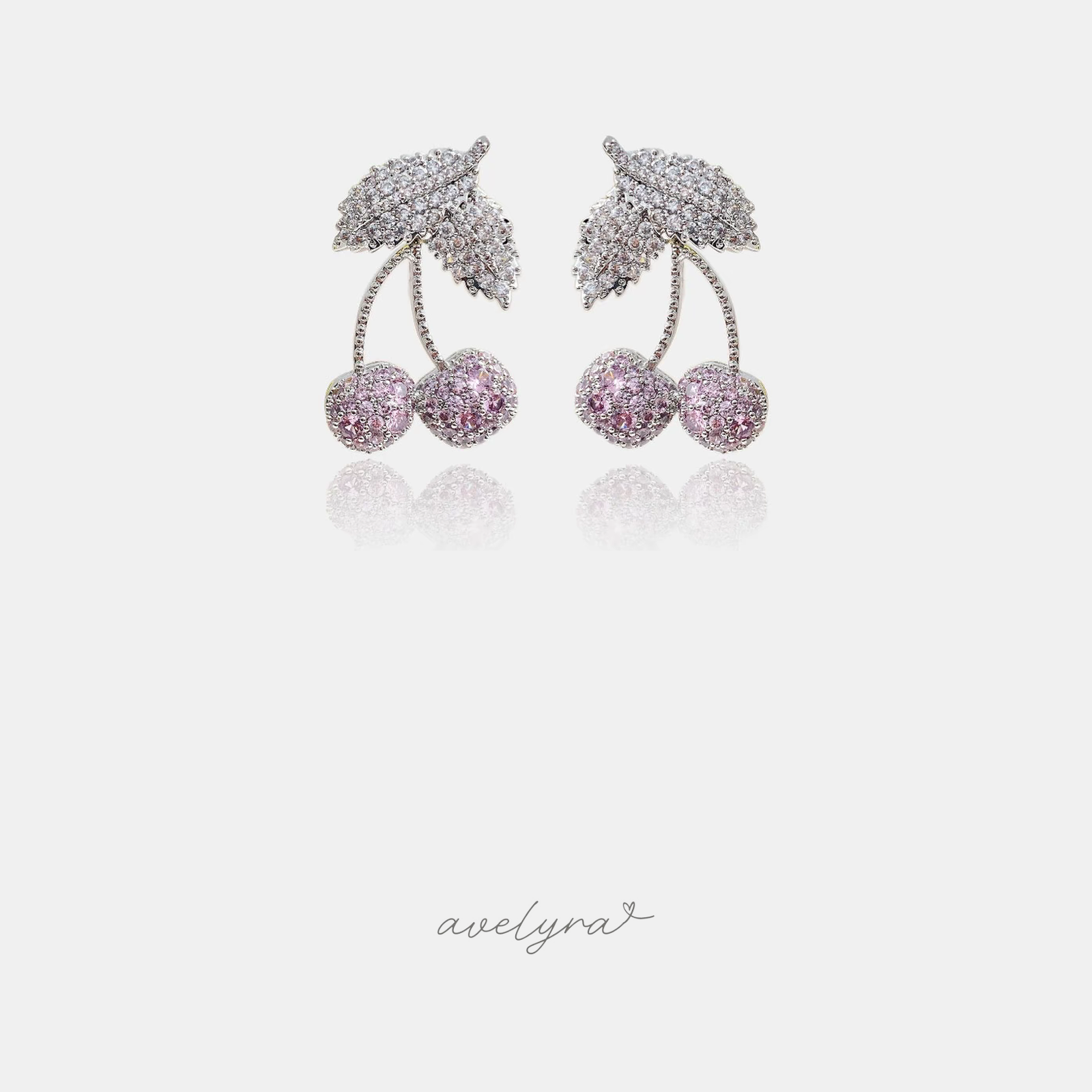 Silver-tone earrings with a pave leaf above two pink pave cherries on curved stems.