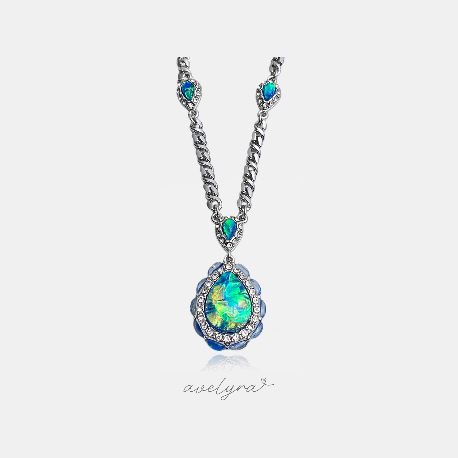 Silver chain necklace with crystal-framed blue-green teardrop stones and a large iridescent teardrop pendant edged with pale-blue cabochon petals in a crystal halo.